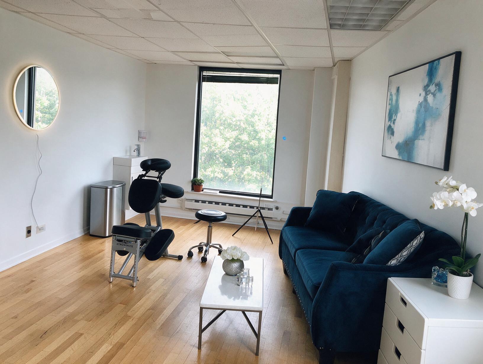 Modern clinic treatment room with comfortable seating, ergonomic chair, natural light, and contemporary decor.